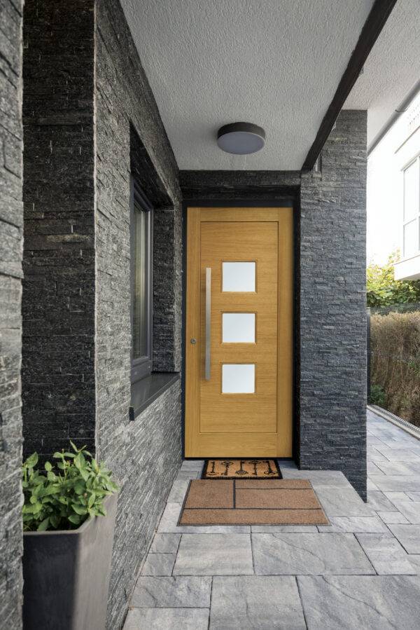 Modern house entrance with a wooden door and stone walls.