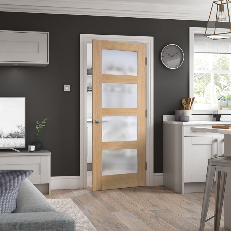 Modern interior with a wooden door with glass panels, gray walls, and kitchen area.