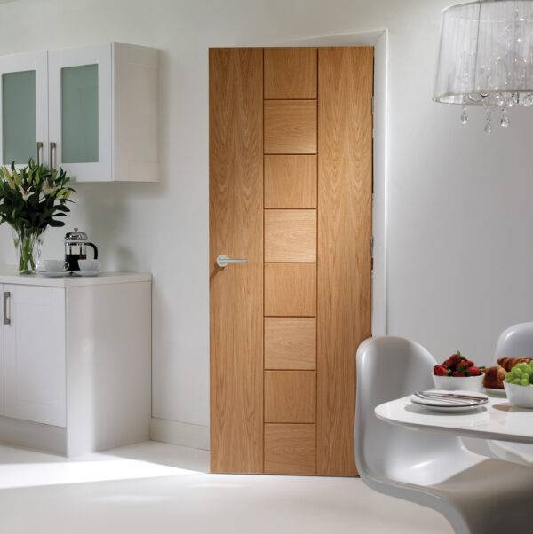 Wooden door in a modern interior setting with kitchen and dining area.