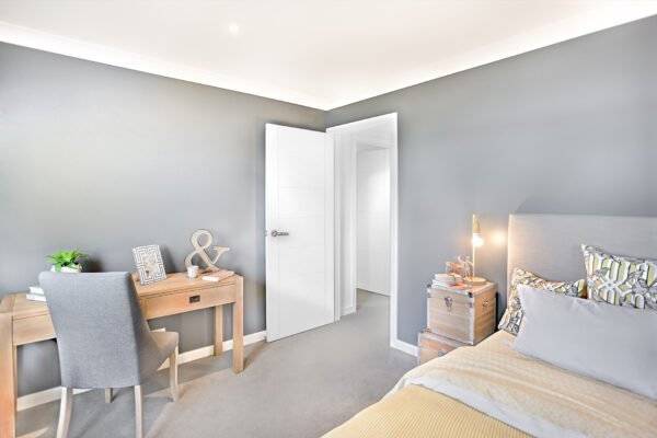 Modern bedroom with a bed, desk, and chair against a gray wall.