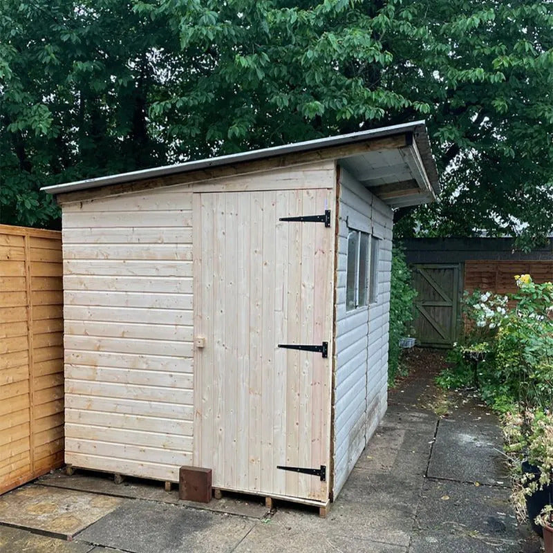 Wooden shed in a garden setting with trees and a wooden fence in the background.